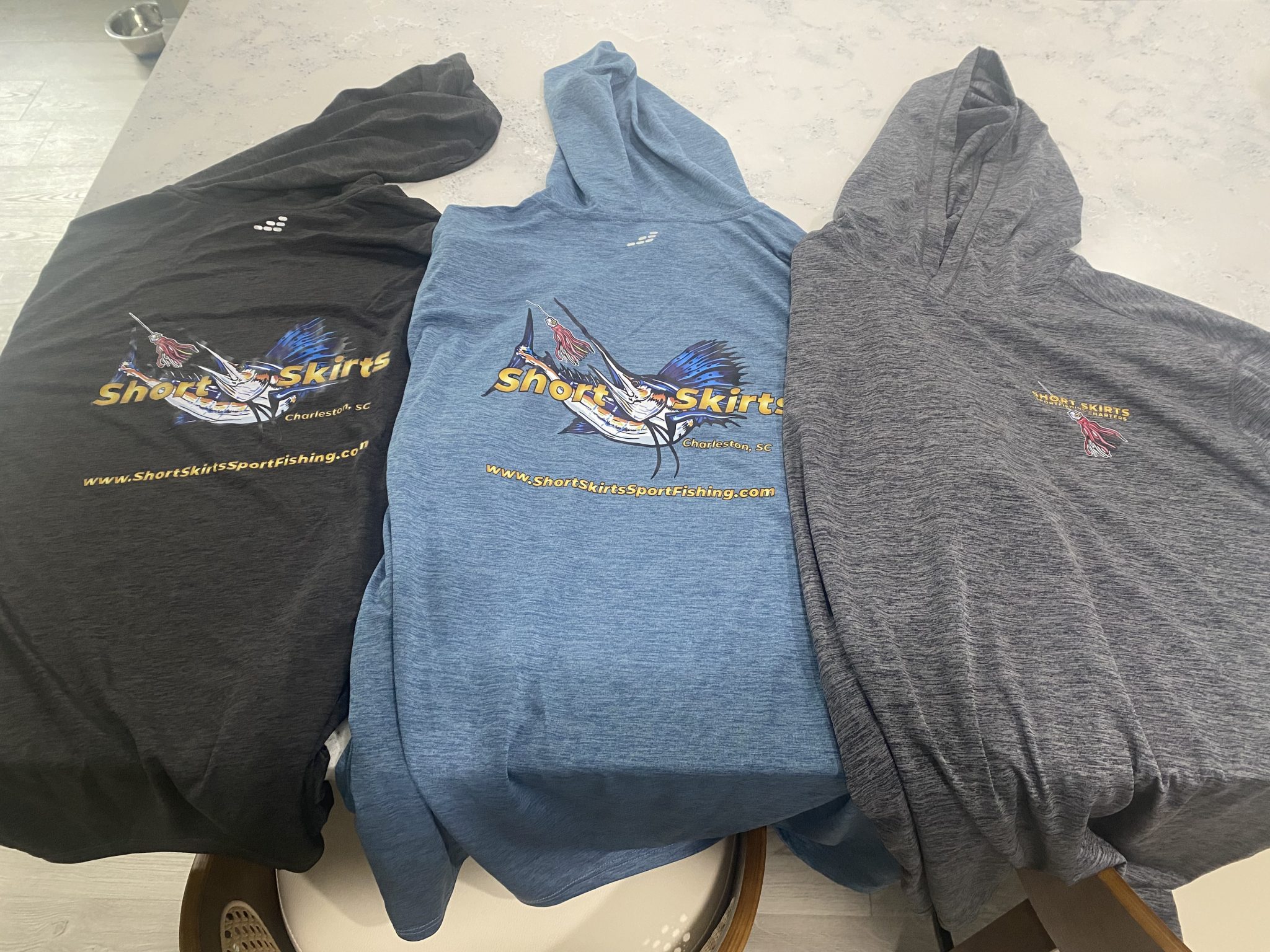 3 different colored Dry-Fit Hoodies for sale with Short Skirts Sportfishing LOGOs